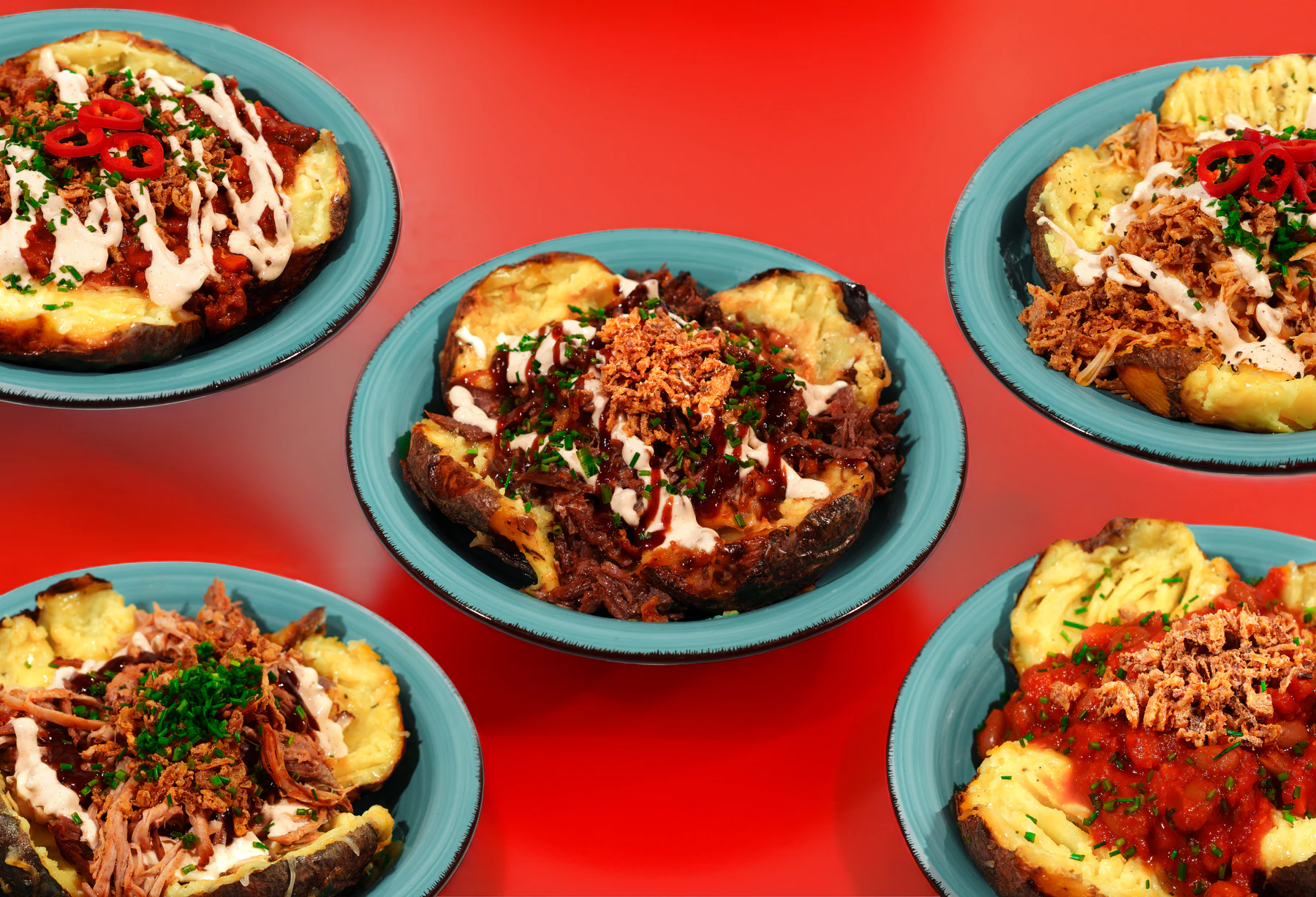Four stuffed baked potato dishes arranged across a saturated red background.