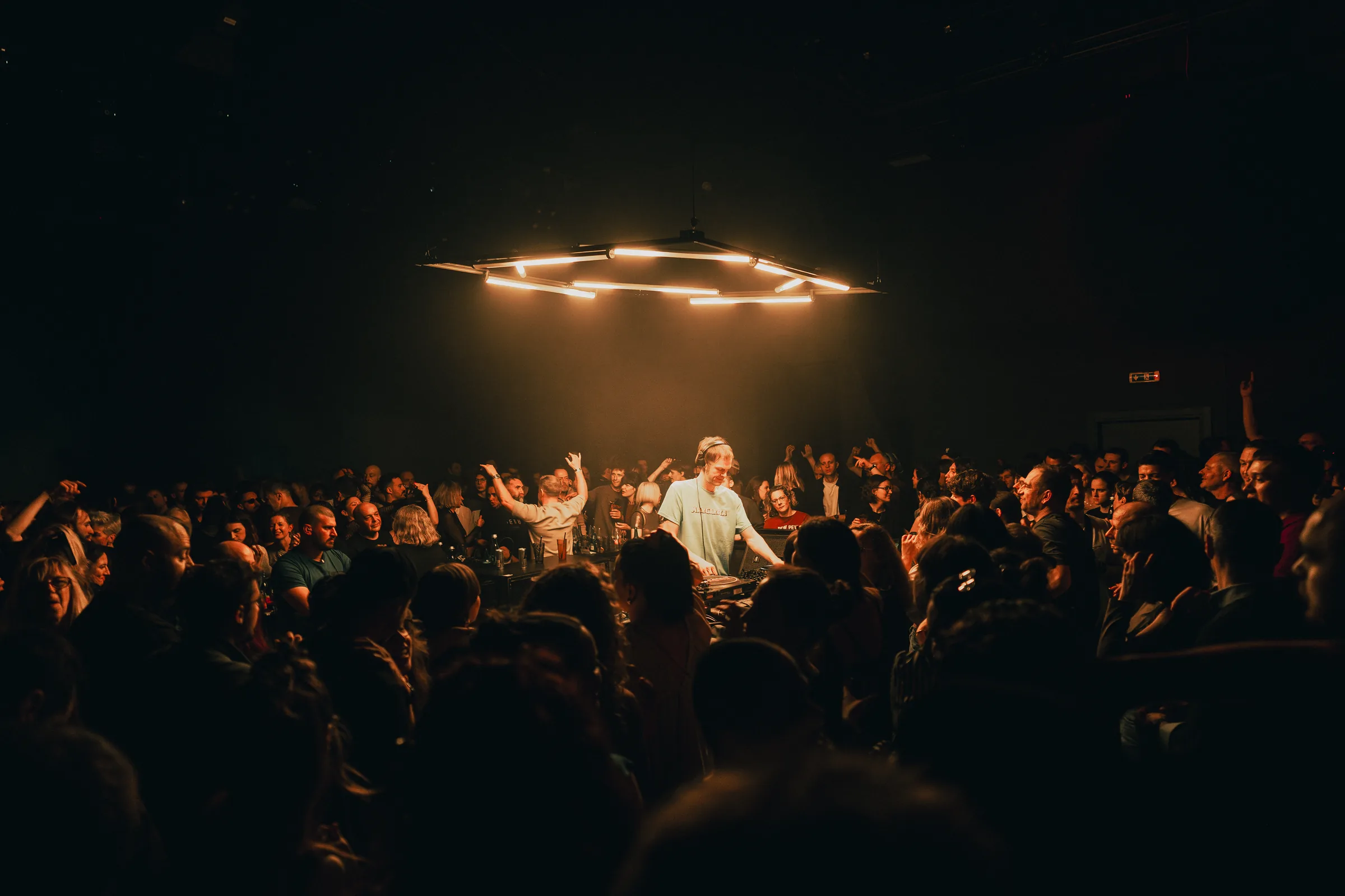 A packed Peti Kupe dance floor seen through warm red and amber light.